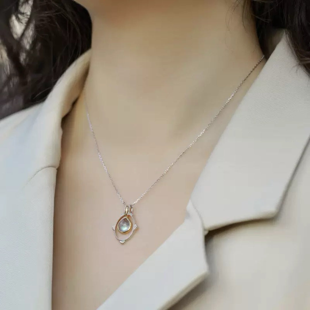 Collier en argent plaqué platine avec un pendentif en forme de larme de labradorite, serti dans un cadre doré orné de petites pierres.