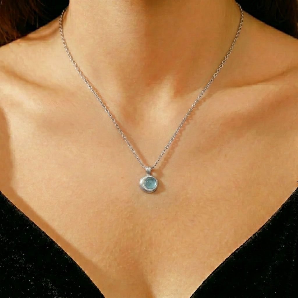Collier en argent avec un pendentif rond en aigue-marine bleutée claire, porté par une femme.