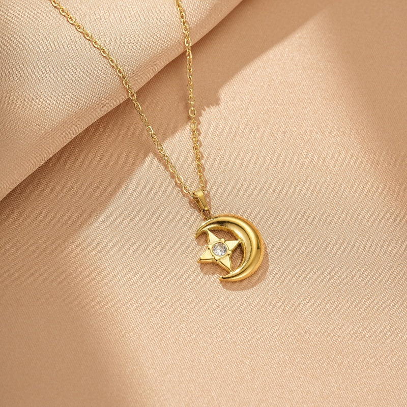 Collier en or jaune avec un pendentif en forme de lune stylisée entourant une étoile sertie d'une petite pierre brillante, le tout sur un fond beige satiné.