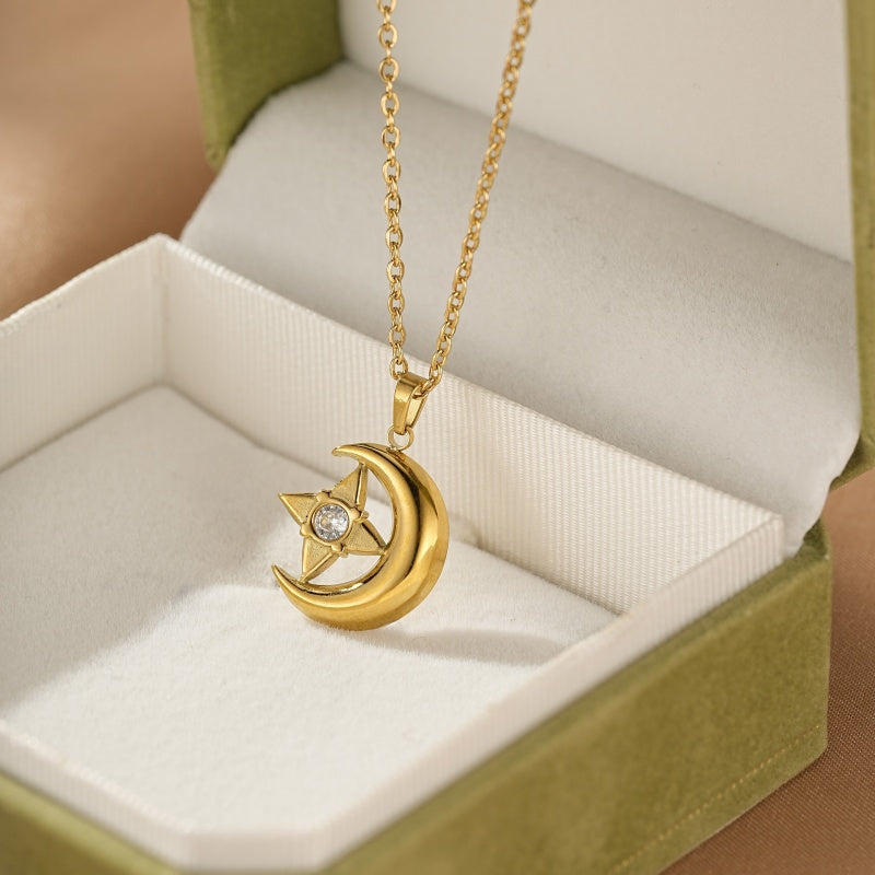Collier doré avec pendentif en forme de croissant de lune et d'étoile orné d'une pierre scintillante, présenté dans une boîte cadeau verte.