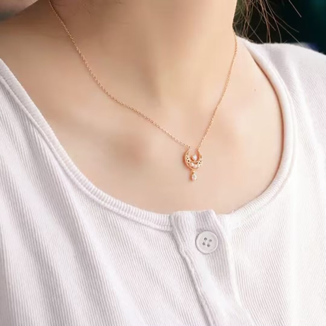 Collier en argent plaqué or avec un pendentif en forme de croissant de lune orné de petites perles et d'une gouttelette scintillante, porté par une femme.