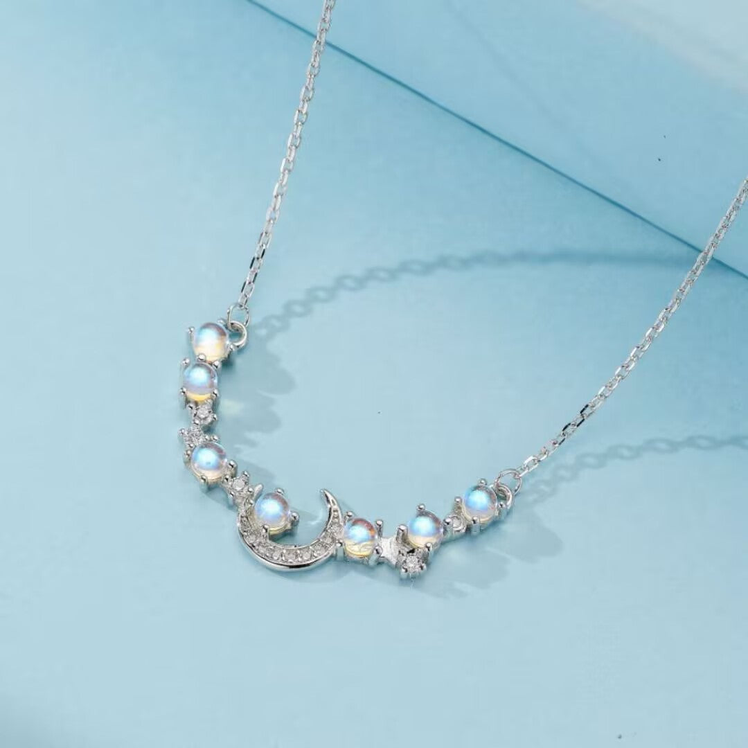 Collier en argent orné d'une lune stylisée et de plusieurs pierres de lune rondes, sur un fond bleu clair.