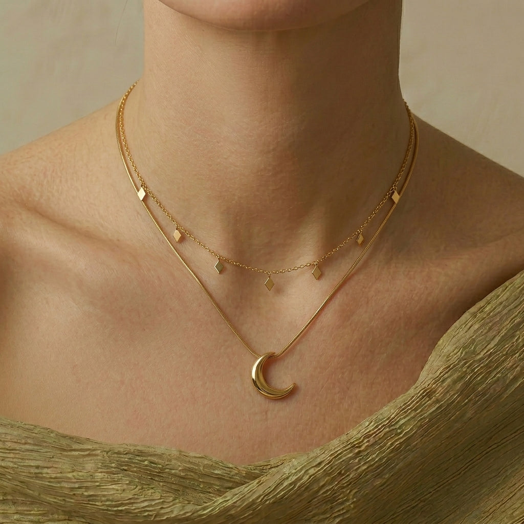 Collier plaqué or à deux rangs avec une chaîne supérieure ornée de petits losanges et une chaîne inférieure avec un pendentif en croissant de lune poli.