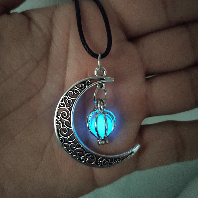 Collier pendentif lune ornementale avec une perle sphérique fluorescente bleu clair dans une cage métallique argentée, sur un cordon noir.