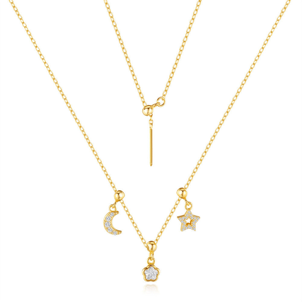 Collier plaqué or avec pendentifs lune, étoile et fleur ornés de zircons cubiques, sur fond blanc.