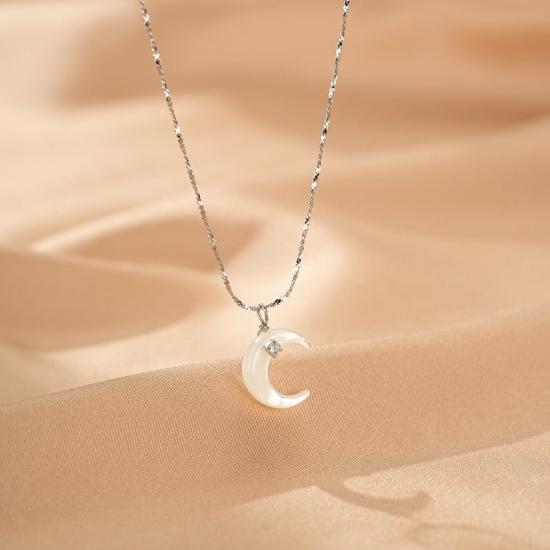 Collier en argent avec un pendentif en nacre en forme de croissant de lune orné d'une petite pierre scintillante.