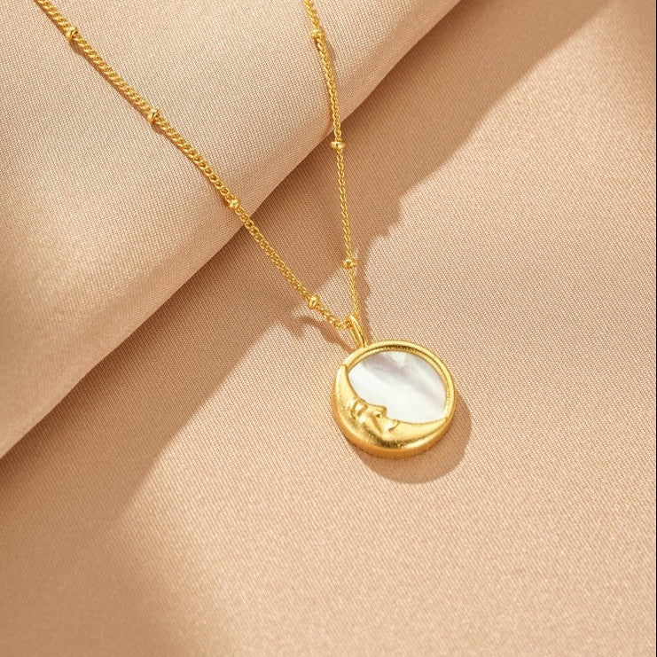 Collier en or avec un pendentif rond en nacre représentant une lune au visage endormi, chaîne délicate avec de petites perles.