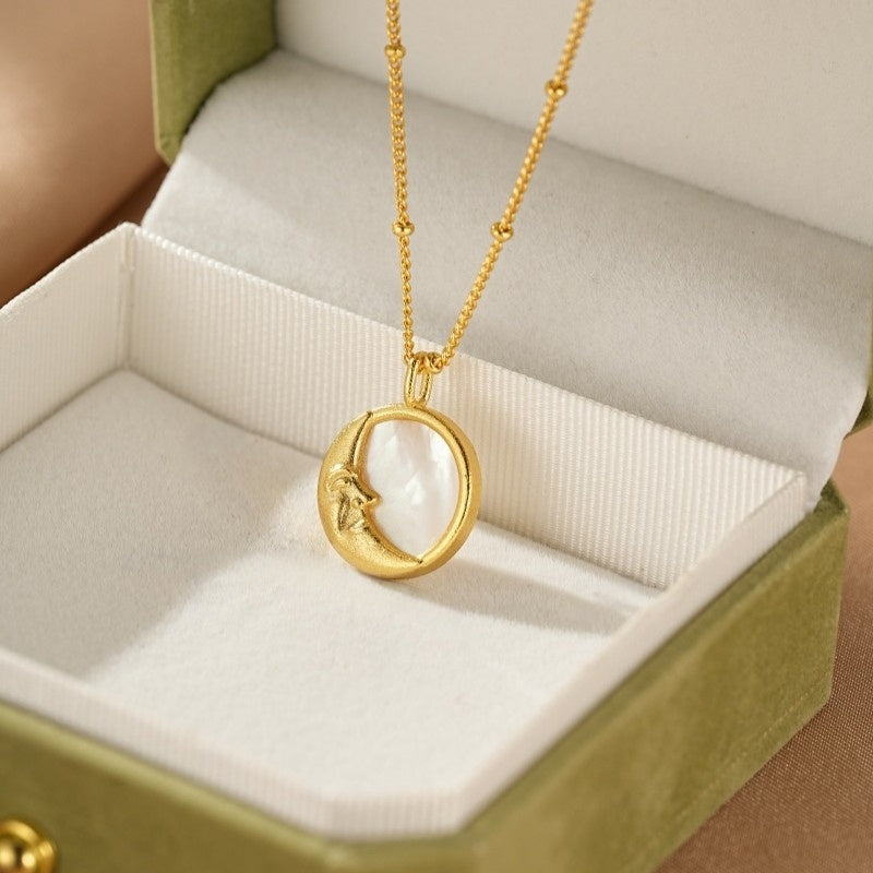 Collier en or plaqué avec un pendentif en nacre représentant une lune de croissant sculptée, dans une boîte cadeau verte.