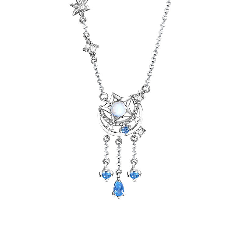 Collier en argent avec un pendentif en forme de croissant de lune orné d'une pierre de lune centrale, de petites pierres bleues et d'étoiles scintillantes, avec des pampilles pendantes ornées de pierres bleues en forme de goutte et de trèfle.