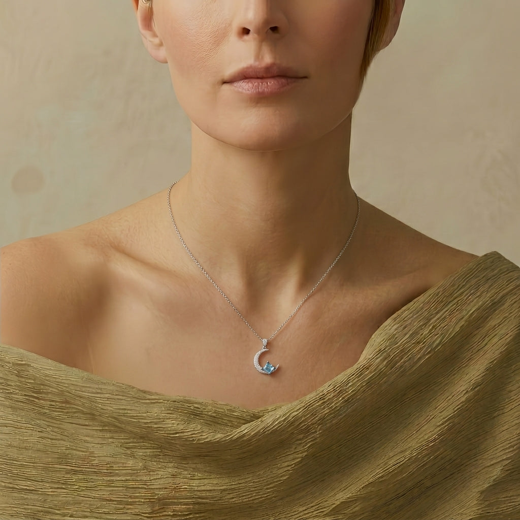 Collier en argent avec un pendentif en forme de croissant de lune orné de petites pierres bleues et blanches, porté par une femme.