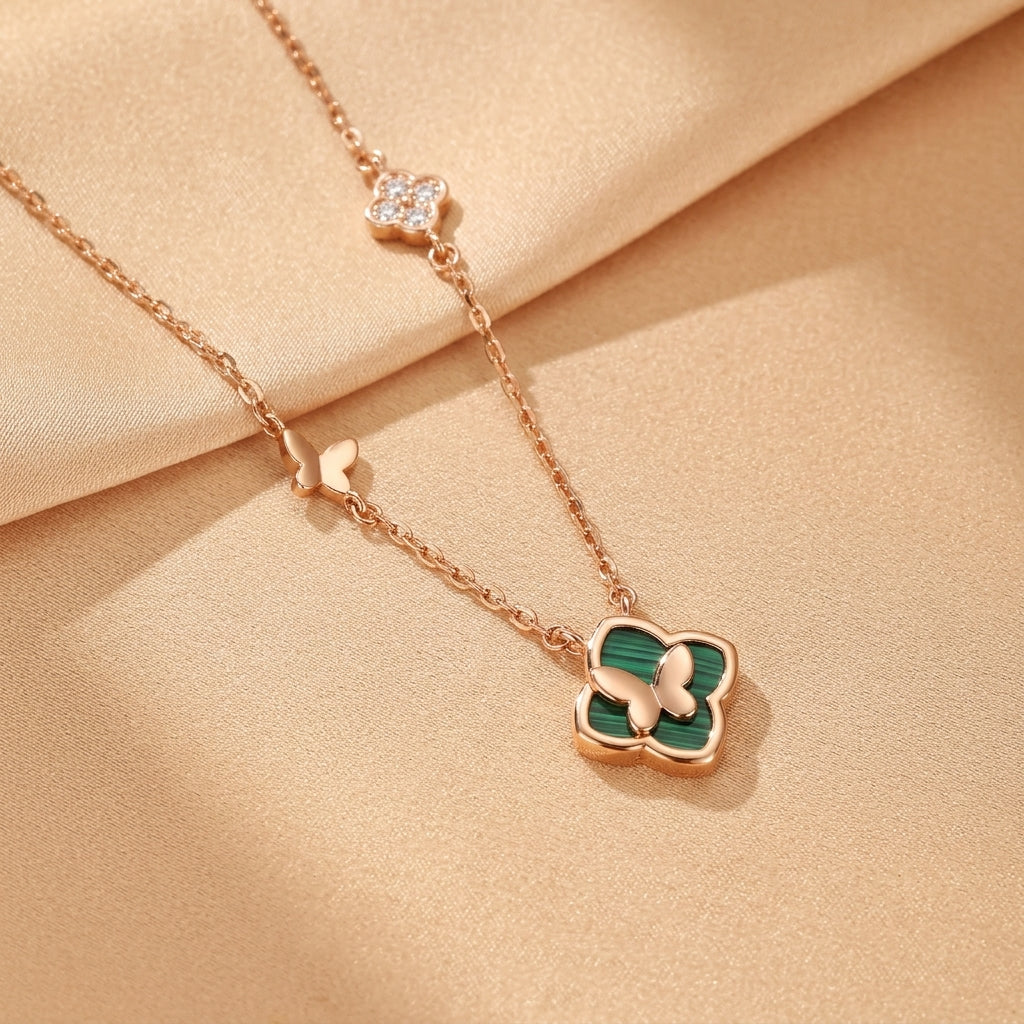 Collier en argent plaqué or rose avec un pendentif trèfle en malachite et un petit papillon doré, orné de petites fleurs et papillons sur la chaîne.