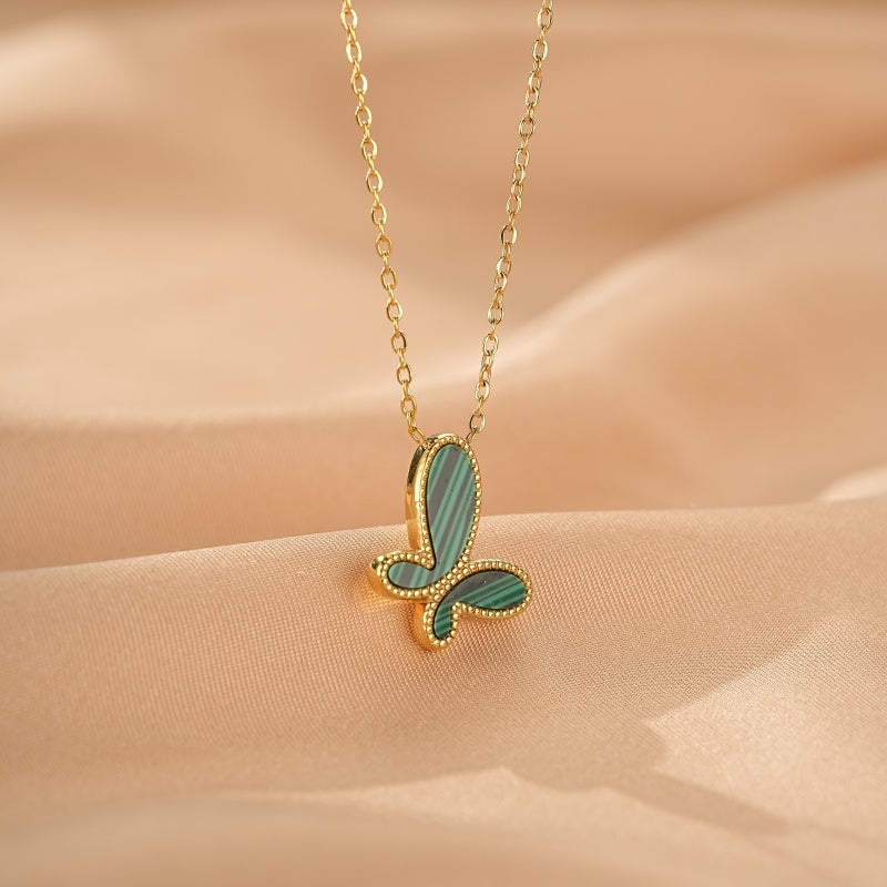 Collier en or avec un pendentif papillon en malachite verte rayée, sur un fond de tissu satiné beige