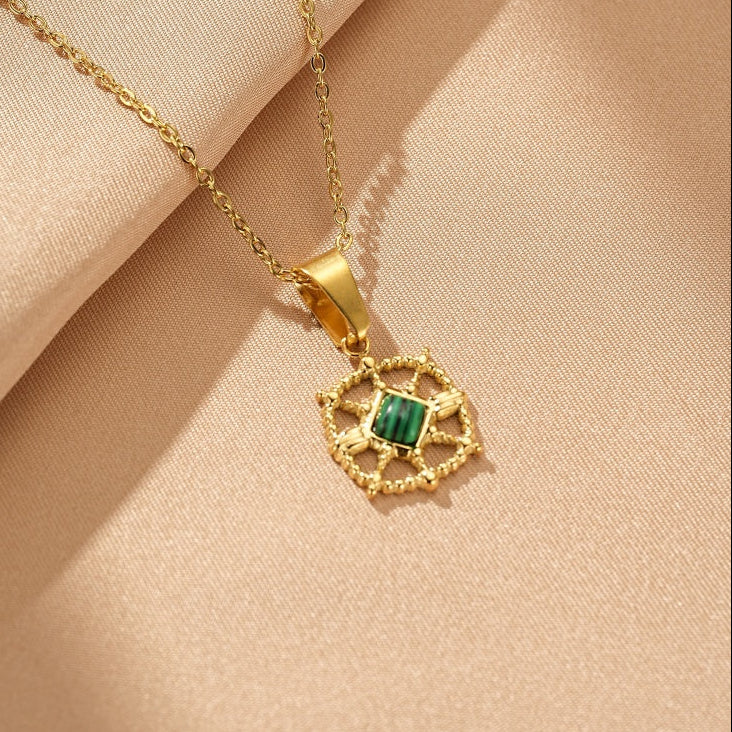 Collier en or avec un pendentif carré serti d'une pierre de malachite verte, sur un fond texturé beige.