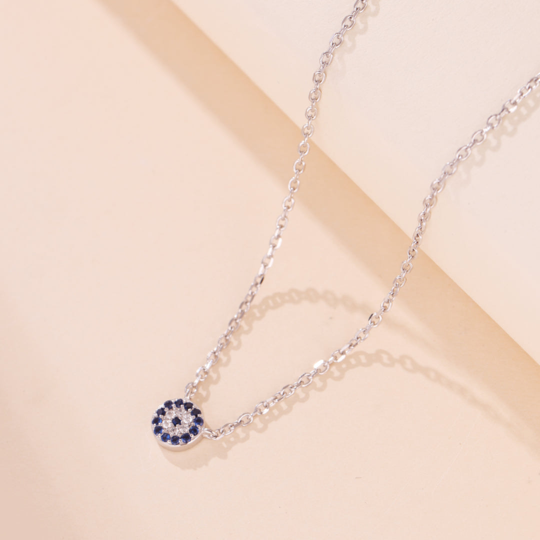 Gros plan sur un collier fin en argent 925 orné d'un pendentif œil bleu et blanc, symbolisant la protection.