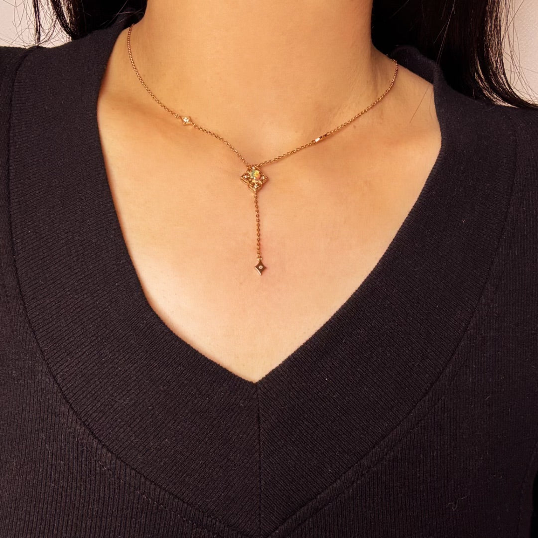 Collier plaqué or avec pendentif en forme de losange orné d'une opale et de petits diamants, porté par une femme.