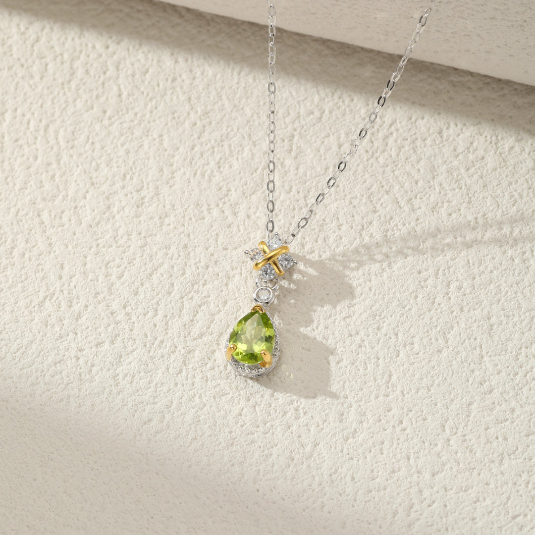 Collier en argent avec une pierre de péridot en forme de poire et un pendentif en forme de croix orné de petits diamants.