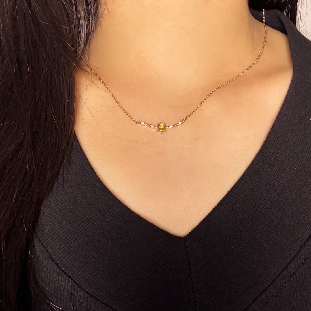 Collier fin en plaqué or avec un pendentif central serti d'une petite pierre verte entourée de cristaux blancs, porté par une femme