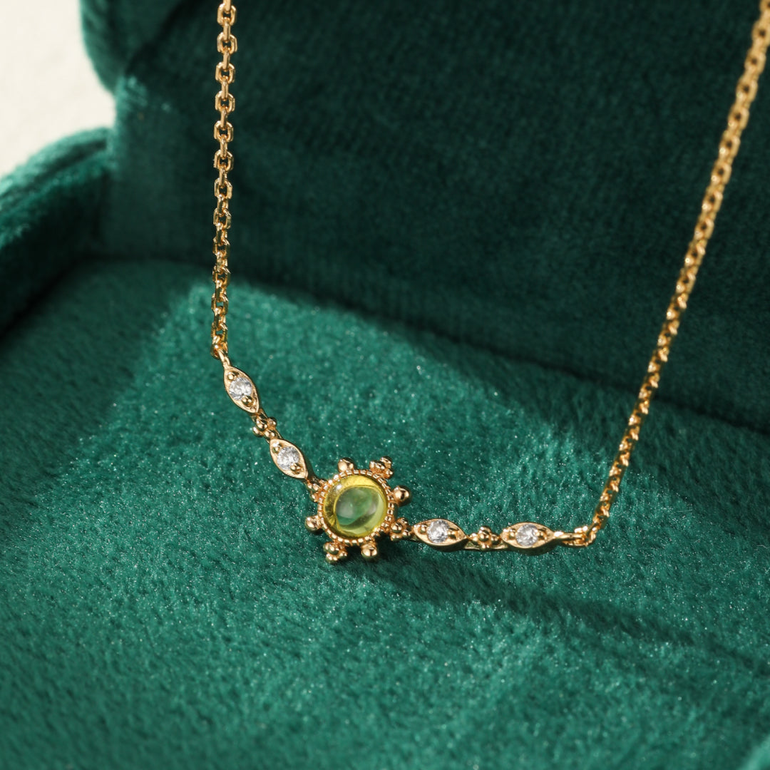 Collier en argent plaqué or avec une pierre centrale péridot verte entourée de petits diamants, sur un fond vert velours.