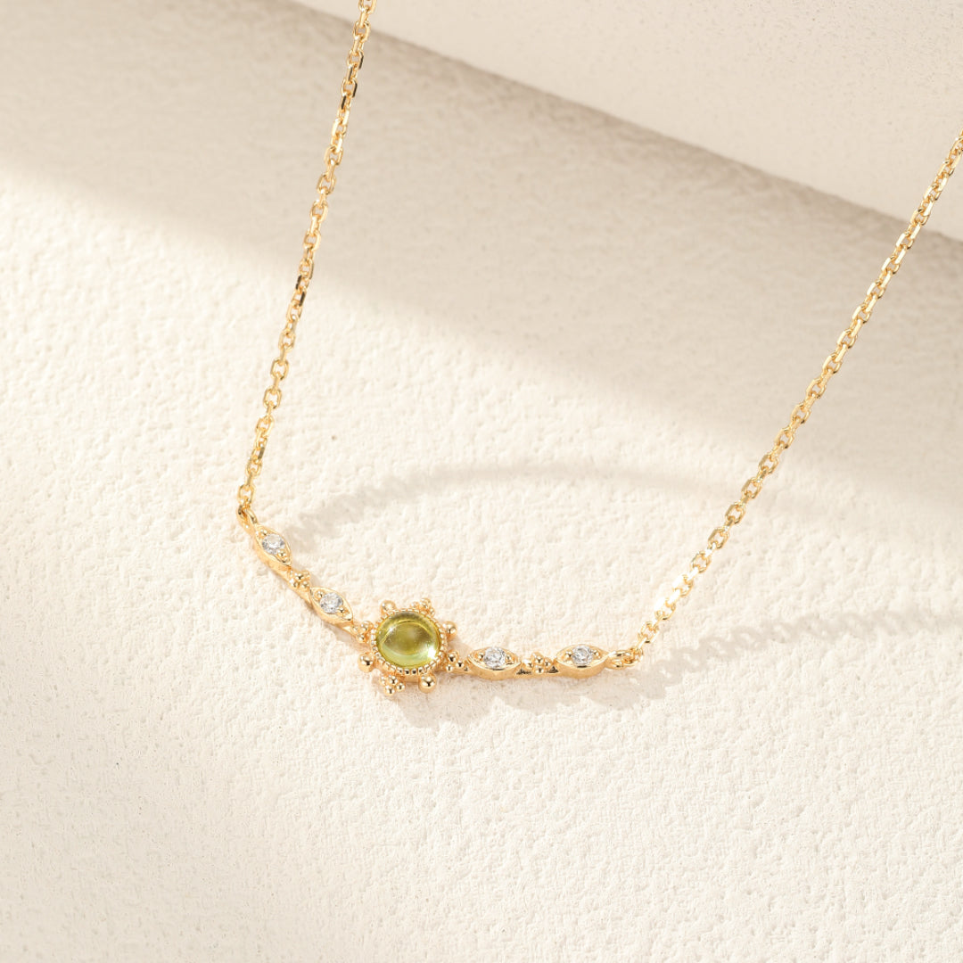 Collier plaqué or avec une pierre centrale péridot ronde entourée de petites pierres blanches, sur une chaîne délicate.