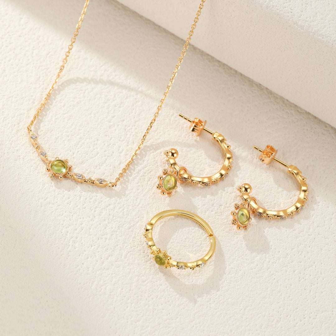 Ensemble de bijoux en argent plaqué or comprenant un collier avec une pierre de péridot et des diamants, des boucles d'oreilles créoles ornées de péridot et des bagues assorties.