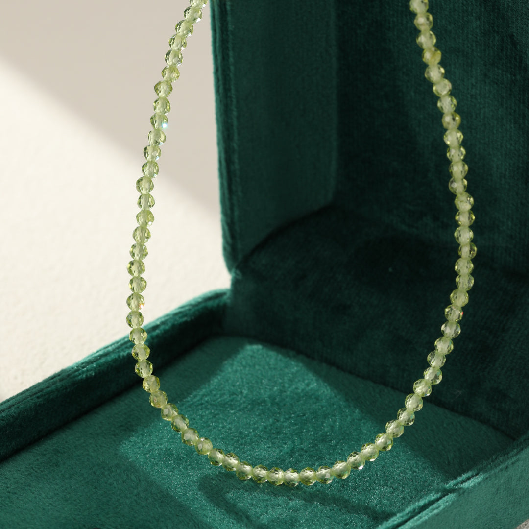 Collier délicat en perles de péridot facetées, dans un écrin vert.