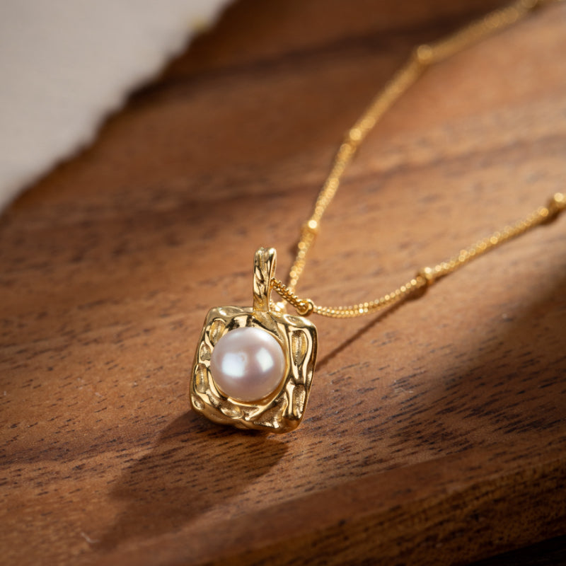 Collier en argent plaqué or avec une perle blanche dans un pendentif carré texturé.