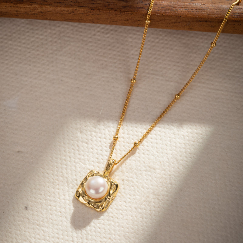 Collier en argent plaqué or avec pendentif carré texturé et perle nacrée.
