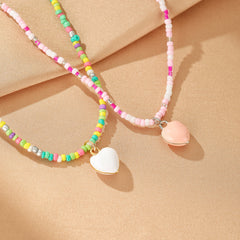 Ensemble de deux colliers de perles de rocaille multicolores avec pendentifs en forme de cœur, un blanc et un rose pâle.