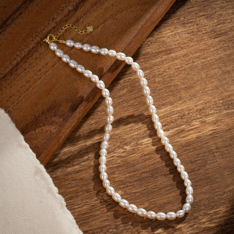 Collier en perles d'eau douce blanches sur fond de bois, avec fermoir en argent plaqué or.