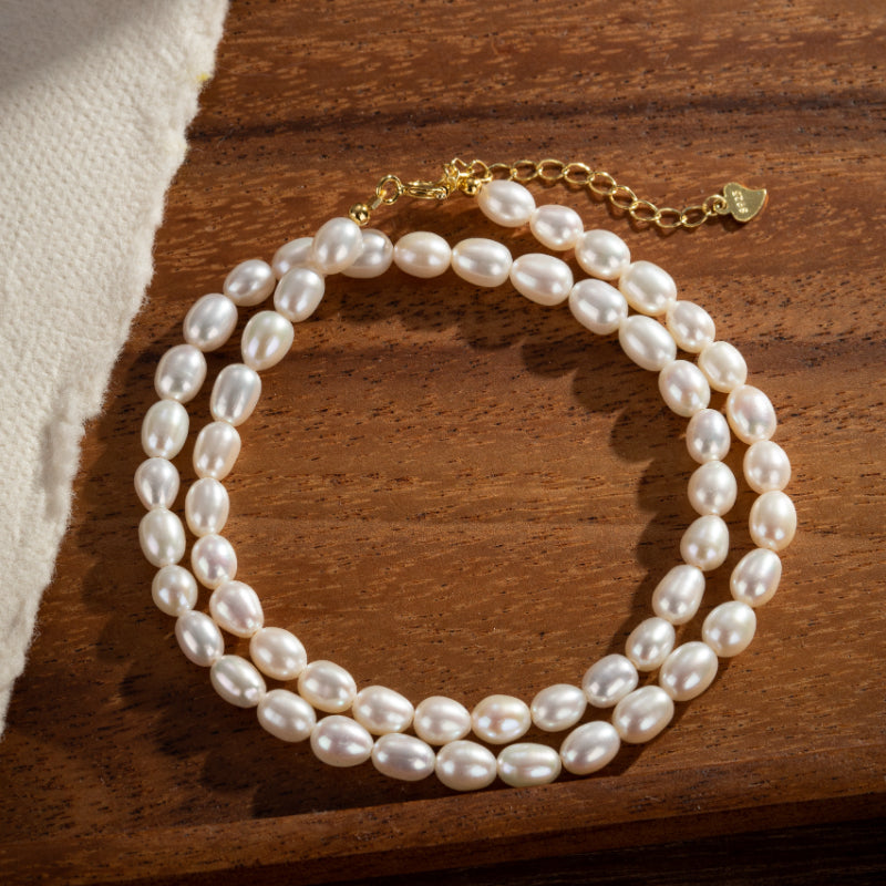 Bracelet double rang de perles d'eau douce blanches sur fond bois avec fermoir plaqué or.