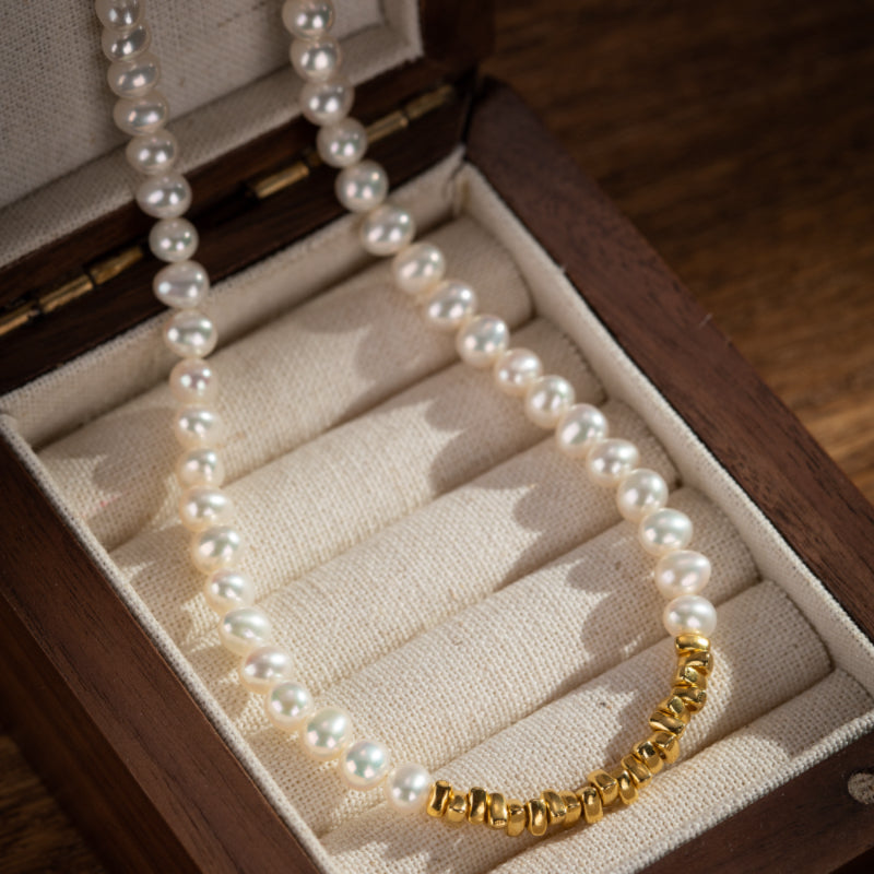 Collier en argent plaqué or avec des perles blanches et des accents dorés texturés, présenté dans une boîte en bois.
