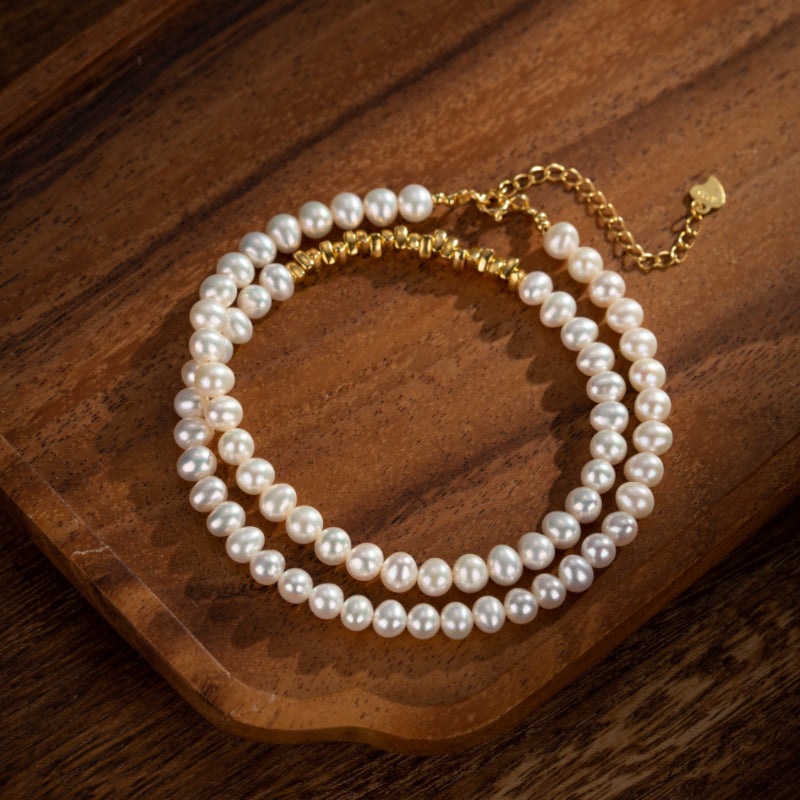 Bracelet double rang de perles d'eau douce blanches, fermoir et chaîne d'extension en argent plaqué or, sur fond en bois.