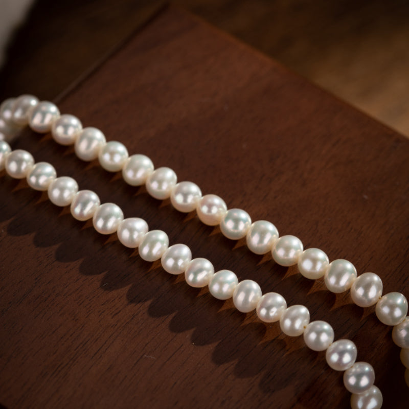 Collier de perles rondes blanches sur fond de bois sombre, bijou artisanal en argent plaqué or
