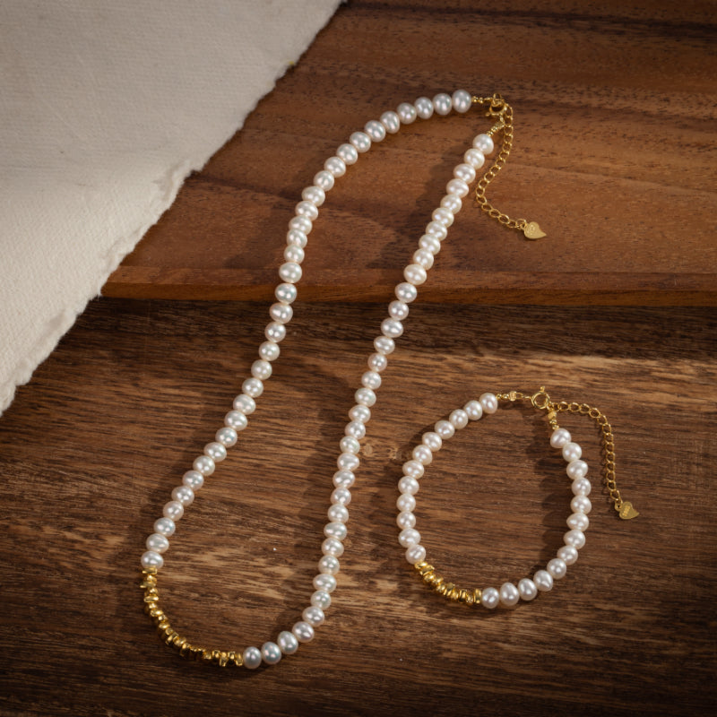 Ensemble collier et bracelet de perles fines sur fond de bois, rehaussé de détails en plaqué or.