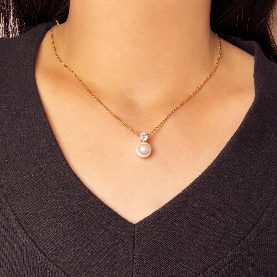 Gros plan sur un collier en or avec une seule perle et un cristal, porté par une femme.