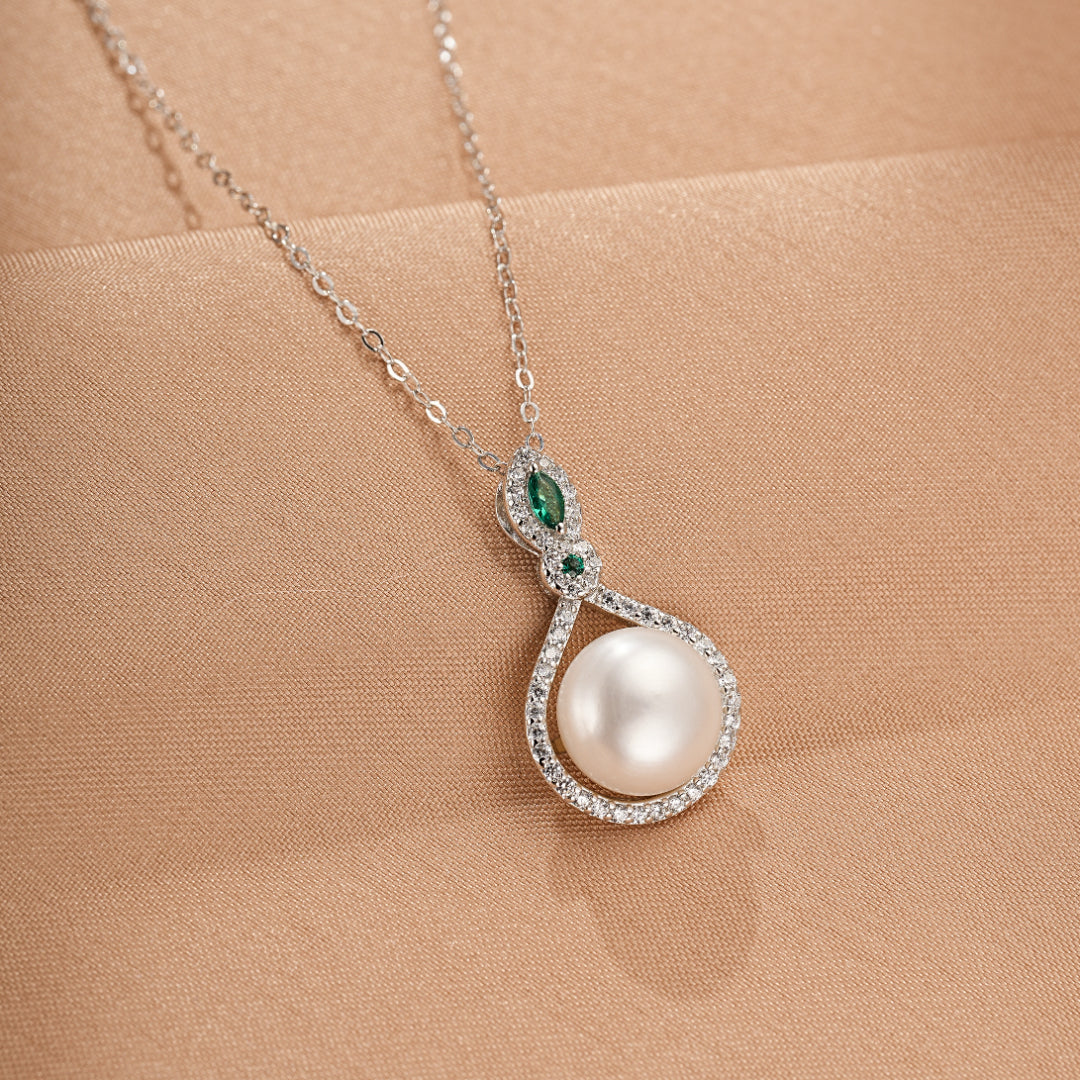 Collier en argent 925 avec une perle ronde nacrée, orné de cristaux scintillants et de deux petites pierres vertes en forme de marquise. Le pendentif a une forme de goutte inversée, symbolisant l'élégance et le raffinement.