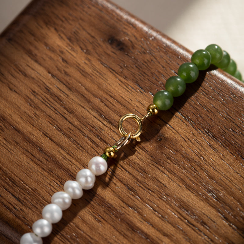 Gros plan sur un collier en perles blanches et jade vert, avec fermoir en plaqué or sur un fond en bois.