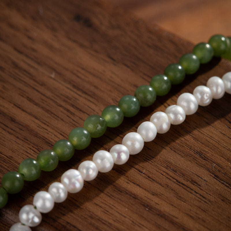 Deux rangées de perles, une de perles blanches et une de perles de jade vertes, sur fond de bois.