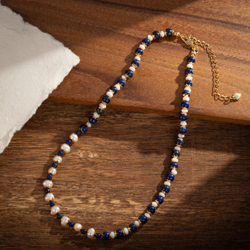 Collier artisanal en perles de lapis-lazuli et perles d'eau douce, monté sur une chaîne plaquée or, sur fond de bois.