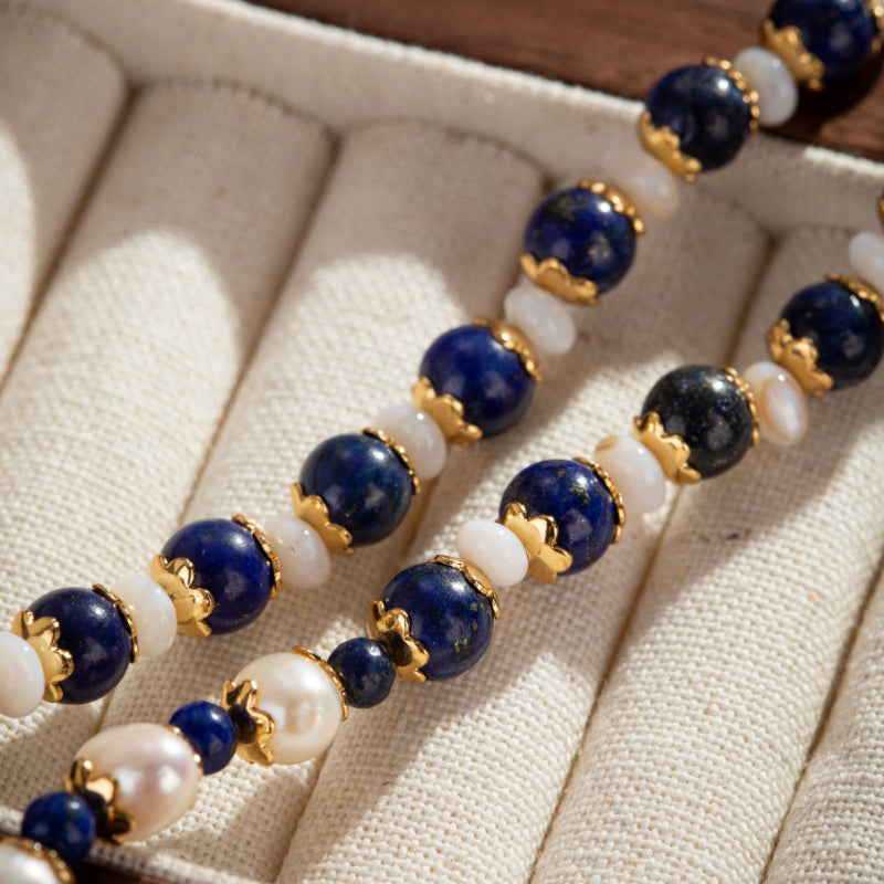 Gros plan sur un collier en perles de lapis-lazuli bleues, perles blanches et perles de culture nacrées, avec des intercalaires dorés.