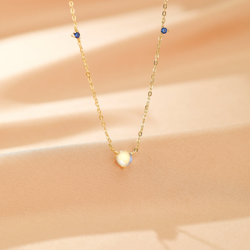 Collier en argent plaqué or 18 carats avec une pierre de lune centrale et de petites pierres bleues rappelant des gouttes célestes.