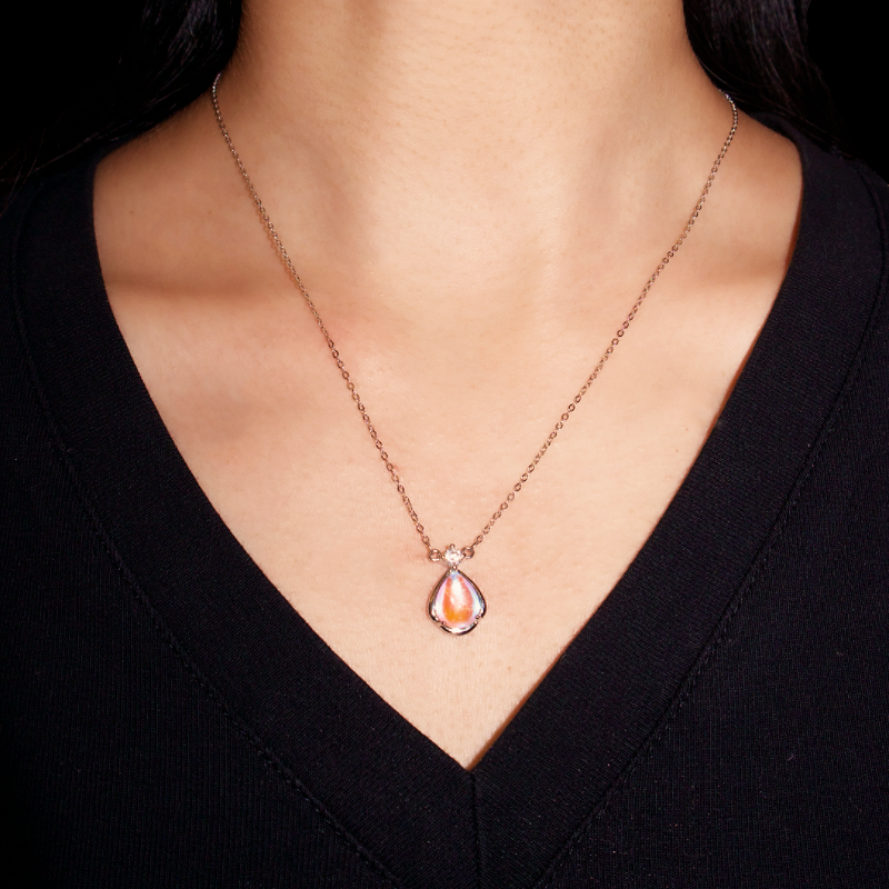 Collier en argent sterling 925 avec un pendentif en forme de larme de pierre de lune aux reflets irisés et nacrés, serti d'une petite pierre cubique de zirconium, porté par une femme.