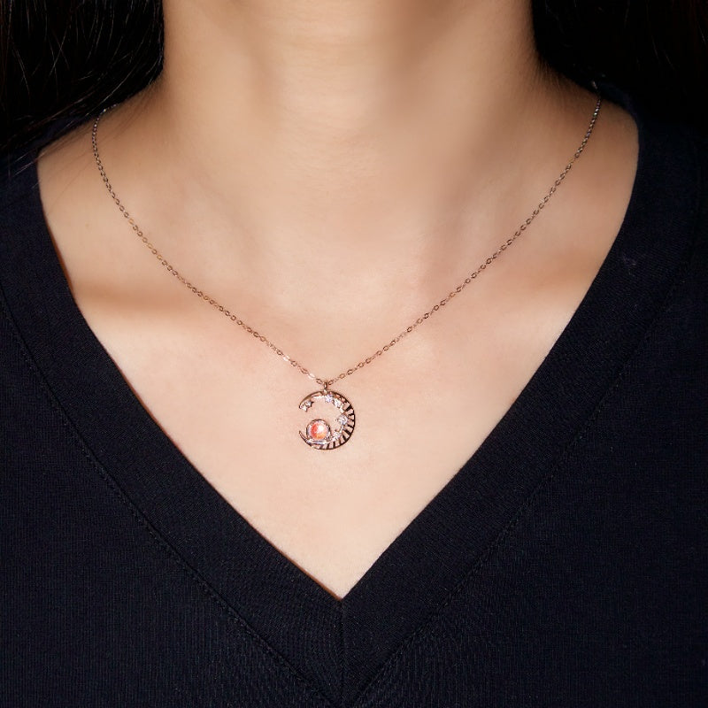 Collier femme avec pendentif croissant de lune argenté serti d'une pierre de lune orange et de petits cristaux scintillants.