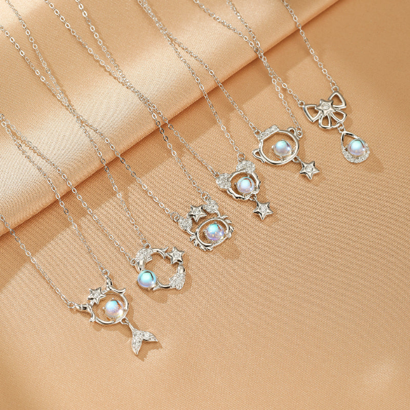 Collection de colliers "Rêve Sidéral" en argent 925, ornés de pierres de lune irisées et de motifs féeriques comme une sirène, des étoiles, un nœud papillon, et un animal stylisé.