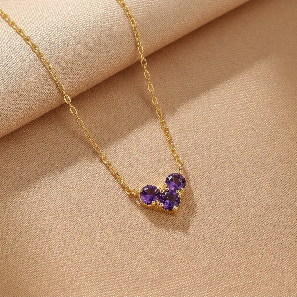 Collier en argent plaqué or avec trois petites pierres violettes disposées en forme de cœur.