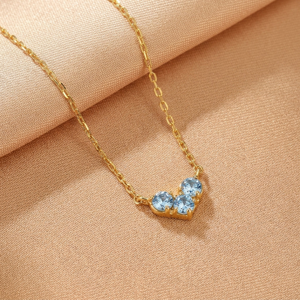 Collier en argent plaqué or avec trois petites pierres bleues disposées en forme de cœur.