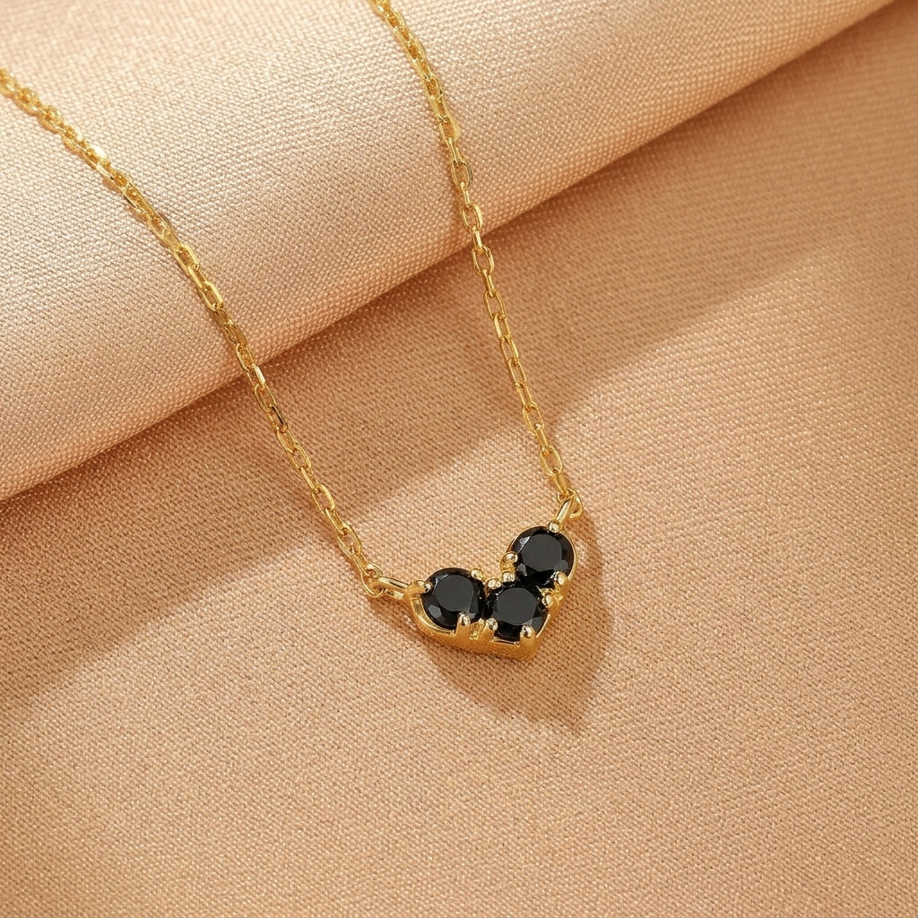 Collier plaqué or avec trois pierres noires formant un cœur sur une chaîne délicate.