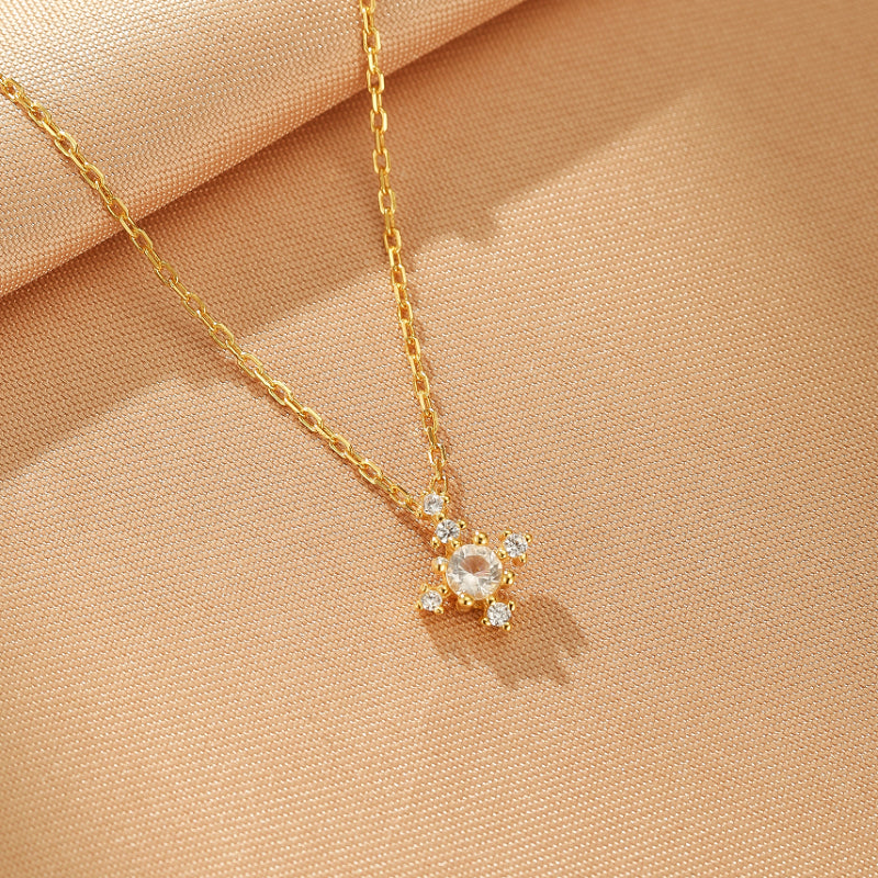 Collier en argent plaqué or avec un pendentif en forme de croix orné de pierres scintillantes, sur fond beige satiné.