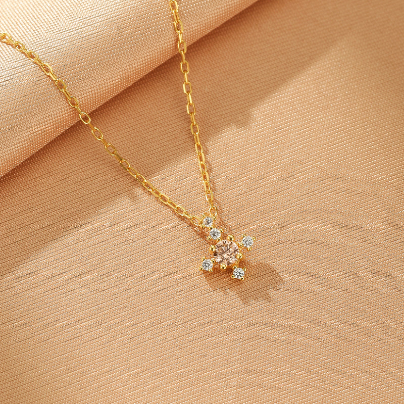 Collier Azur Infini en argent plaqué or, avec une petite croix ornée d'une pierre centrale rose pâle et de petites pierres blanches scintillantes.