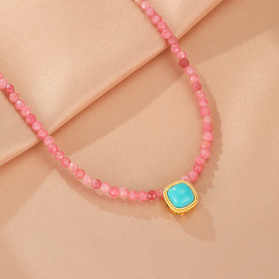 Gros plan sur un collier composé de perles roses facettées et d'un pendentif carré en turquoise rehaussé d'une monture dorée.